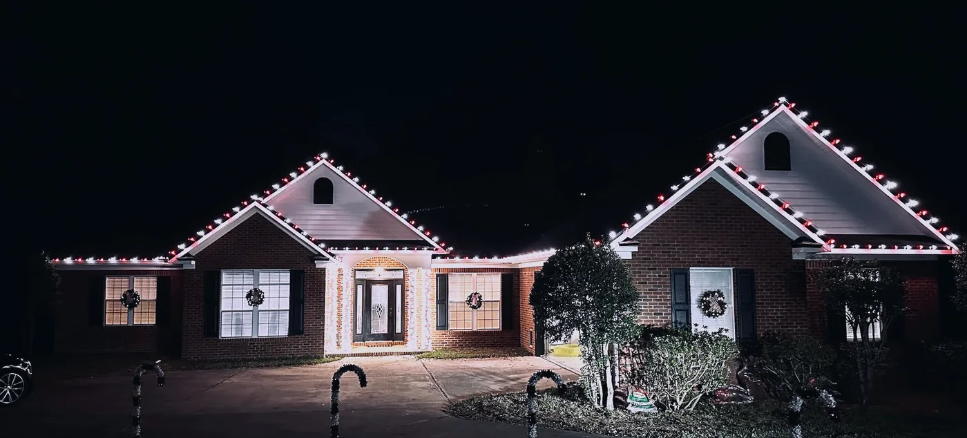 Red and white candy cane Christmas lights on a brick home with lit window wreaths
